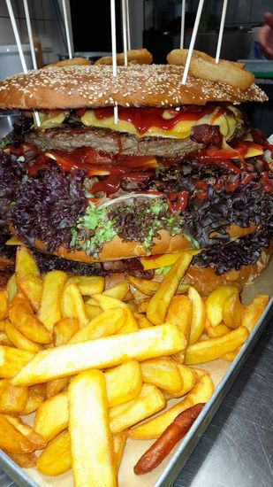 Big Dora Seitenansicht — 3 Patties à 1.200g, Ketchup, lila Salat, Pommes auf dem Tablett
