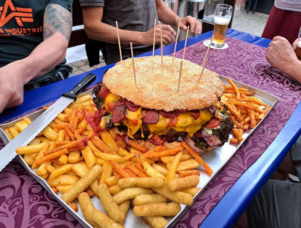 Dora Burger auf dem Tisch — riesiger Burger mit Pommes und Süßkartoffelpommes im Freien